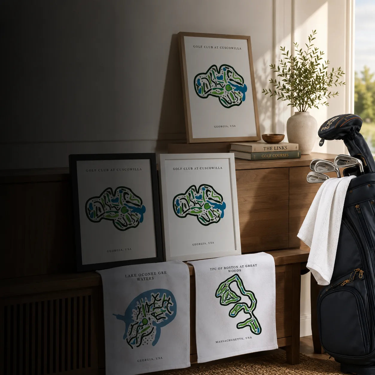 Framed golf course prints and personalized golf towels displayed beside a golf bag