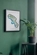 Framed map of Pebble Beach Golf Links on a green wall with a plant on a table below.