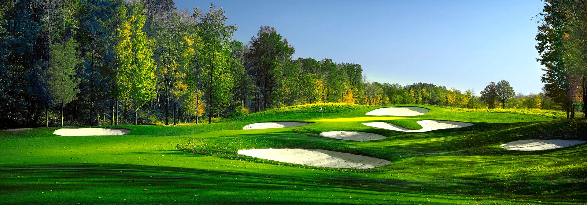 Golf course with green grass, sand bunkers, and trees under a clear blue sky.